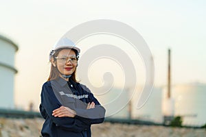 Asian woman engineer arm crossed and smile with confident looking forward to future with oil refinery plant factory in background