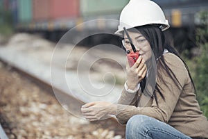 Asian woman engineer or construction worker wearing safety hat helmet and holding portable radio at railway project. Civil