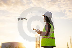 Asian woman engineer operate flying drone over oil refinery plant during sunrise building site survey in civil engineering project