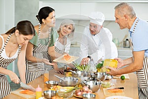 Asian woman engrossed in cooking talking to participants of culinary class