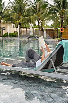 Asian woman enjoy reading book and relaxing at swimming pool