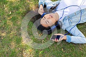 Asian woman enjoying the music while lyuing on the grass in city park - view from the top.