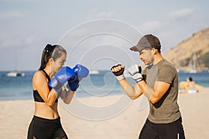 Asian woman and European man train boxing on a tropical beach. Personal training