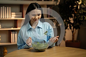 Asian woman Experiencing Disappointment Over Tasteless Salad at Home in the Evening