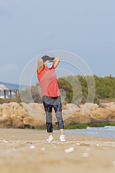 Asian woman with a face mask stretching at the beach