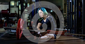 Asian woman is facing overtraining syndrome after weight training workout inside gym with dark background for exercising