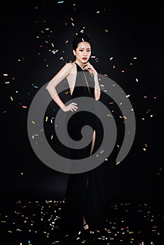 Asian woman with fashion makeup in luxury black dress while confetti falling on her.