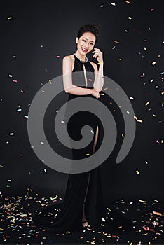 Asian woman with fashion makeup in luxury black dress while confetti falling on her.