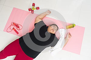Asian woman fat exhausted with excess weight lying on floor after training at home photo