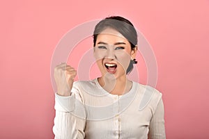 Asian woman feeling happy and excited on accomplish success on pink background.