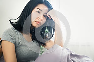Asian woman feeling sad and depressed sitting in bed next to the window