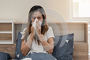 Asian woman feeling unwell and sneezing on the bed