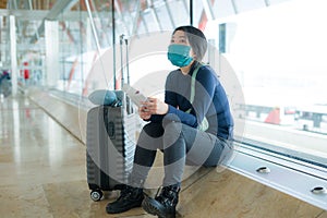 Asian woman flying in covid19 times - young tired and attractive Korean girl in face mask waiting on airport with her flight