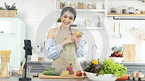 Asian woman food blogger cooking salad in front of smartphone camera while recording vlog video and live streaming at home in