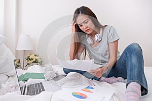 Asian woman freelancer headache about paperwork on bed with laptop in bedroom.work at home concept.stress working.