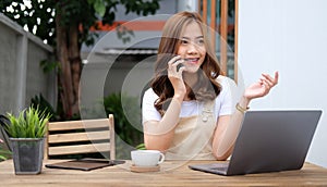 Asian woman freelancer sitting at outdoor cafe and talking on mobile phone with her business partner