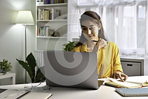 Asian woman freelancer working on computer at home. Attractive businesswoman studying online, using laptop software