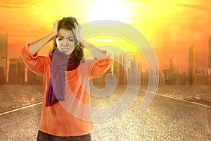Asian woman getting a headache because of the heatwave on the city with glowing sun background photo