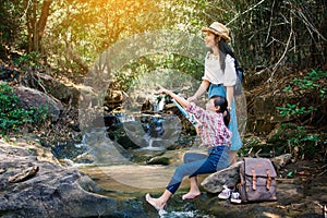 Asian woman and girl looking a map sitting on the rock near waterfall in forest background