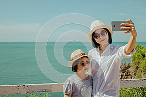 Asian woman and girl standing relax on cliff nearly seashore, They taking selfie together.