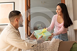 Asian woman giving gift box to man in living room