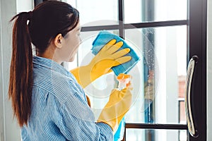 Asian Woman in gloves cleaning solution Spraying and cleaning the window House keeping concept