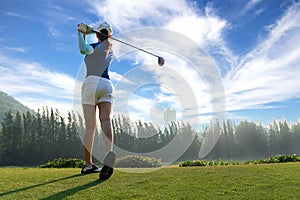 Asian woman golf player doing golf swing tee off on the green evening time in the blue sky background. She presumably does exerci