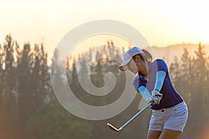 Asian woman golf player doing golf swing tee off on the green sunset evening time,