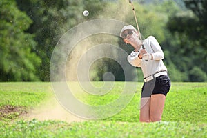 Asian woman golfer hitting a bunker shot