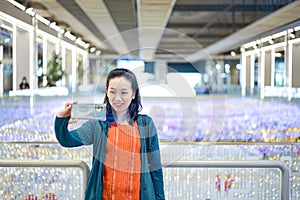 Asian Woman in green orange cloth selfies in shopping mall which is a colorful light place