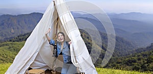 Asian woman greeting friend while on a solo trekking camp on the top of the mountain with small tent for weekend activities and