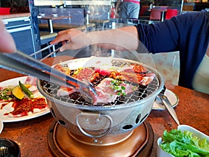 Asian woman grilled raw sliced beef and pork on the hot stainless steel stove with smoke