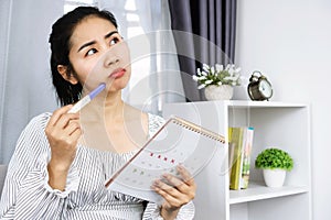 Asian woman hand holding calendar and pregnancy test counting the date and checking her menstrual cycle planning for ovulation