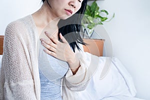 Asian woman hand holding chest pain, difficulty to breathe, heartburn from acid reflux after wake up in bed