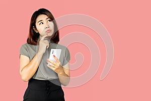 Asian woman hand holding smart phone wonder, thinking and planning something standing over pink background