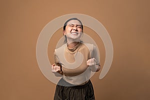 Asian woman happy make a winning gesture  on beige background
