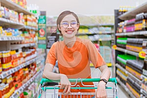Asian woman happy shopping in shopping mall handle shopping cart around with supermarket shelf