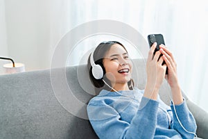 Asian woman of happy smiling are listening to music from white headphones and using hands touch smartphone.