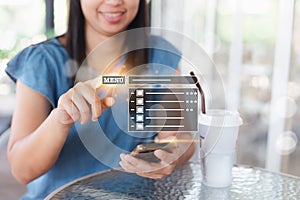 Asian woman happy to order food online by touching on menu virtual screen in the restaurant.