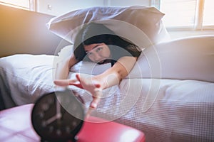 Asian woman hates getting stressed waking up early,Female stretching her hand to ringing alarm to turn off alarm clock