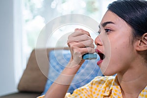 Asian woman having an asthma attack using an asthma inhaler at home