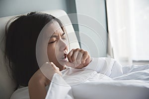 Asian woman having a cold. Girl is coughing on her bed. Illness, disease concept.