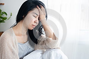 Asian woman having headache migraine, hangover, lack of sleep sitting in bed after wake up in morning