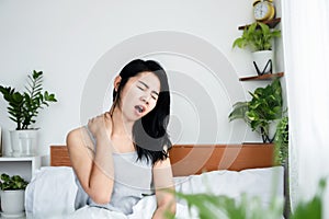 Asian woman having neck pain, sore muscle, shoulder and back ache sitting in bed after wakeup in morning