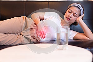 Asian woman having painful stomach ache,Female suffering from abdominal pain,Period cramps or premenstrual syndrome lying on sofa photo