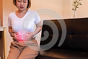 Asian woman having painful stomach ache,Female suffering from abdominal pain,Period cramps or premenstrual syndrome sitting on sof