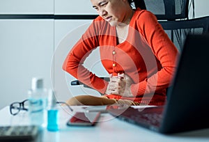 Asian woman having painful stomach ache during working at home,Female suffering from abdominal pain,Period cramps,Hands squeezing