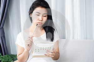 Asian woman having problem with amenorrhea, irregular periods looking at calendar and counting her menstrual cycles photo