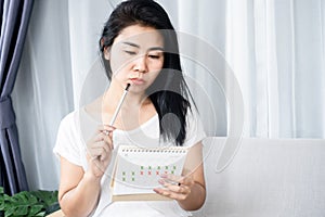 Asian woman having problem with amenorrhea, irregular periods looking at calendar and counting her menstrual cycles