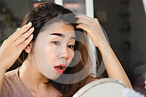 Asian woman having problem with grey hair looking at the mirror